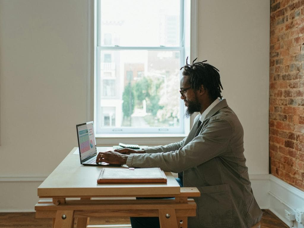A man sitting and working on a laptop in a warm office setting.